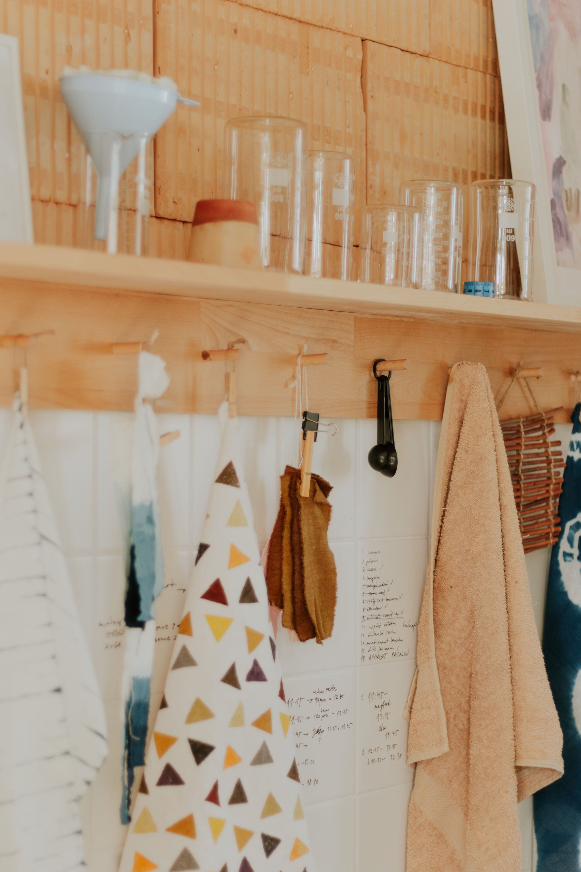 Wooden shelf with various items including a patterned apron, kitchen utensils, and towels in DOT 'N' POT natural dye studio